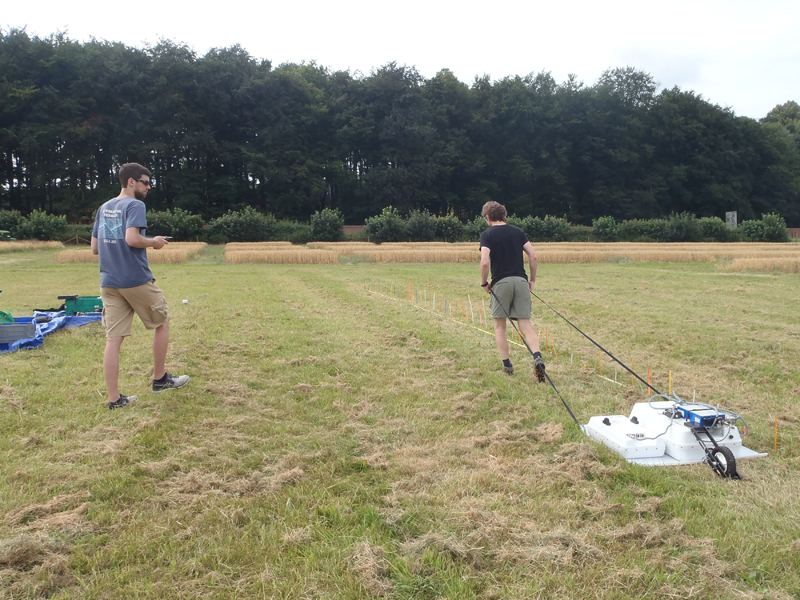 Researcher pulling device through grassy field.